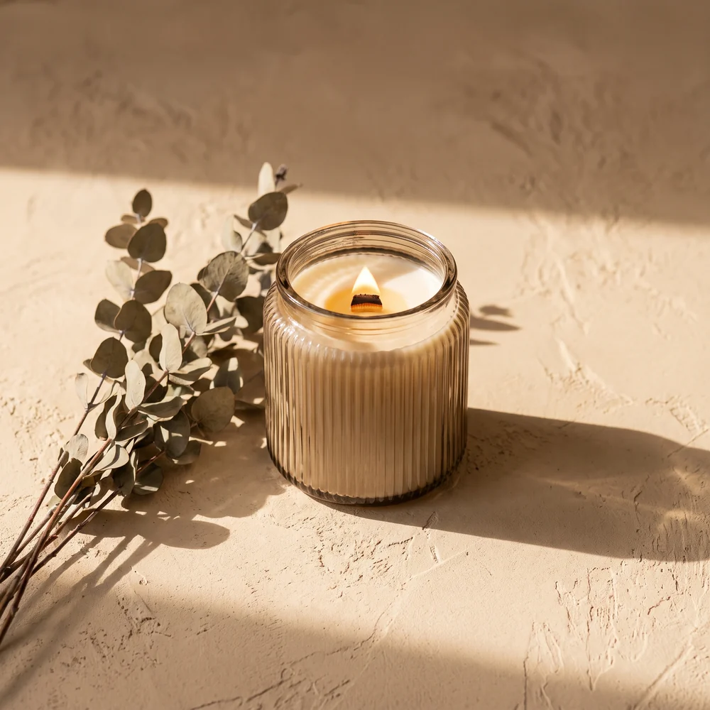 Glass candle styled on a textured surface with dried stems